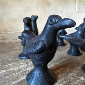 May include: A collection of small, black bird figurines. Each bird has a detailed beak, eye, and wing design. The figurines are arranged on a textured surface, showcasing their unique shapes and forms. These decorative pieces add a touch of nature-inspired art.