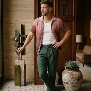 Può includere: Una persona indossa una camicia a maniche corte con bottoni con una sfumatura di colore dal rosso al marrone, una maglietta bianca e pantaloni a pieghe verde scuro. La persona indossa anche mocassini neri.