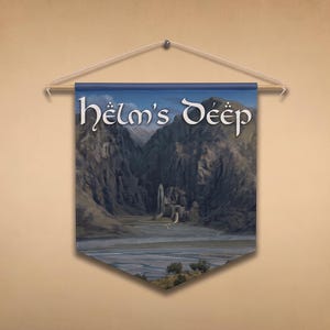 May include: A rectangular fabric wall banner featuring a printed illustration of a mountain valley landscape with a fortress structure. The text "Helm's Deep" is printed in a stylized white font at the top. The banner hangs from a wooden rod.