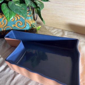 May include: A ceramic tray with an irregular, angular shape. The interior surface is finished in a smooth, glossy dark blue glaze, while the exterior walls feature a natural, matte terracotta finish with a slightly wavy, textured surface.