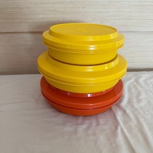 May include: A stack of three round plastic storage containers with lids. The top two containers are bright yellow, while the bottom container is a vibrant orange. Each container features a smooth, matte finish and a secure, flat-fitting lid.