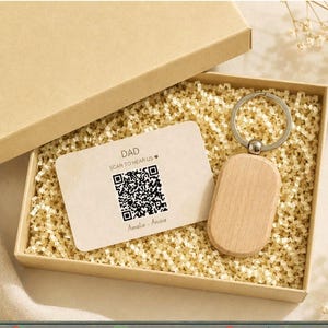 May include: A gift box with a wooden keychain and a card that says "DAD SCAN TO HEAR US" with a QR code. The keychain has a silver ring and a light brown, oval-shaped wooden tag. The card is light brown with black text.