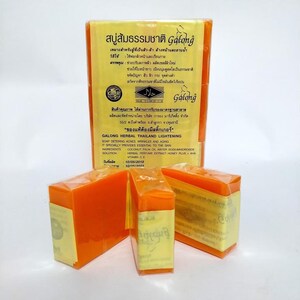 May include: Several orange herbal soap bars, wrapped in clear plastic, with text in Thai and English. The soap is labelled "Galong Herbal Thailand Lightening" and is designed to address acne, wrinkles, and aging. The packaging includes a Halal certification.