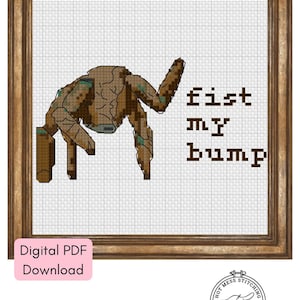 Może przedstawiać: Wzór do haftu krzyżykowego w drewnianej ramie. Projekt przedstawia brązową, stylizowaną postać z napisem "fist my bump" brązowymi literami. Słowa "Digital PDF Download" znajdują się w różowym pudełku.