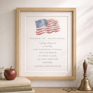 Può includere: Stampa incorniciata con il testo del Giuramento di Fedeltà e una bandiera americana ad acquerello. La stampa è in una cornice di legno chiaro. Una mela, libri, una campana e chiavi sono in primo piano.