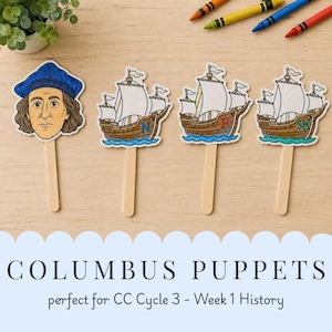 May include: Four paper puppets on wooden sticks featuring a portrait of Christopher Columbus and three sailing ships labeled with the letters N, P, and SM. The illustrations are colored with markers and arranged on a light wood surface with crayons.