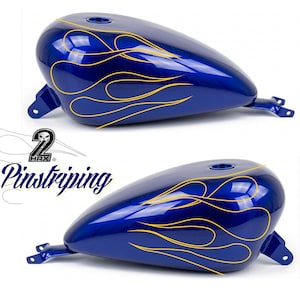 Peut inclure: Deux réservoirs d'essence bleus pour moto avec des motifs de flammes jaunes. Les réservoirs ont une finition brillante et sont posés sur un fond blanc. Le texte "2 Hax Pinstriping" est visible.