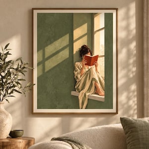 May include: A framed wall art print depicting a person with dark hair in a bun, wearing a striped robe, sitting in a window frame and reading an open red book. The scene features sage green walls, warm sunlight casting window pane shadows, and a neutral frame.