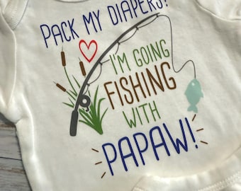Könnte beinhalten: Weißer Baby-Body mit dem Text "PACK MY DIAPERS! I'M GOING FISHING WITH PAPAW!" in Blau und Braun. Eine Angelrute, ein Herz und ein Fisch sind ebenfalls abgebildet.