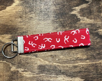Könnte beinhalten: Roter Stoffschlüsselanhänger mit einem silbernen Schlüsselring. Der Stoff hat ein weißes Hufeisenmuster.