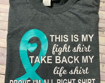 May include: A dark grey t-shirt with a teal ribbon and white text that reads "THIS IS MY fight shirt TAKE BACK MY life shirt PROVE I'M ALL RIGHT SHIRT".