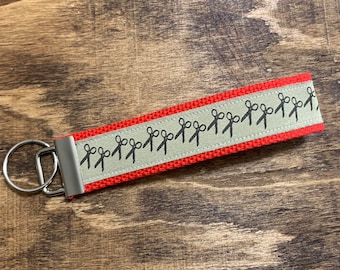 May include: Red and gray key chain with a silver key ring. The key chain has a repeating pattern of black scissors.