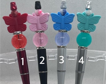 May include: Four pens with butterfly toppers. The pens are red, black, silver, and silver. The butterfly toppers are red, pink, blue, and turquoise. The pens are numbered 1 through 4.