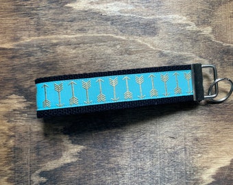May include: A black and blue key chain with a gold arrow pattern. The key chain has a silver metal ring.