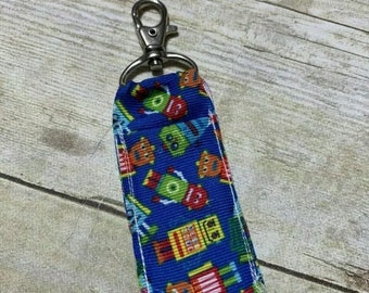 May include: A blue and white key chain with a pattern of robots. The key chain has a silver metal key ring.