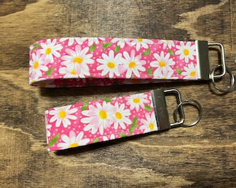 May include: Pink and white daisy patterned fabric key chain with a silver key ring.