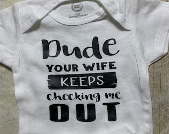 Könnte beinhalten: Weißer Baby Strampler mit schwarzem Text, der "Dude your wife keeps checking me out" lautet.