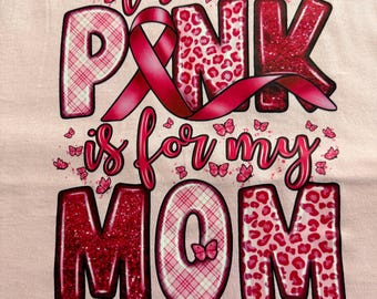 Könnte beinhalten: Ein hellrosa T-Shirt mit dem Text "the PINK is for my MOM" in großen, gemusterten Buchstaben. Das Design enthält eine rosa Schleife, verschiedene Rot- und Rosatöne, Leopardenmuster, Karomuster, Glitzereffekte und kleine rosa Schmetterlinge als Akzente.