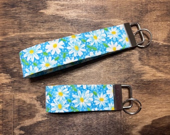 May include: Two keychains with a blue and white daisy print fabric. The keychains have silver metal key rings.