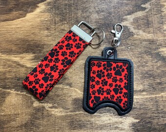 May include: A red and black paw print patterned fabric key chain with a black fabric hand sanitizer holder attached.