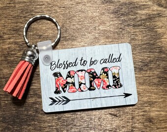 Könnte beinhalten: Ein rechteckiger Schlüsselanhänger mit dem Text "Blessed to be called MIMI" in schwarzer Schrift und floralem Druck. Der Schlüsselanhänger hat einen silbernen Schlüsselring, einen transparenten Kunststoffclip und eine korallenfarbene Quaste.