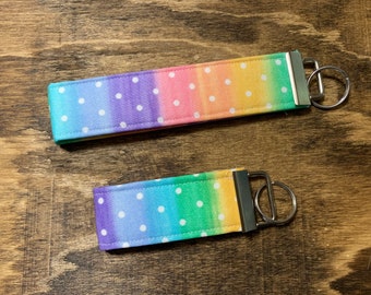 Könnte beinhalten: Zwei Schlüsselanhänger mit einem Regenbogen-Farbverlauf und weißen Punkten. Die Farben gehen von Lila über Blau, Grün, Gelb bis hin zu Orange. Jeder Anhänger hat einen silberfarbenen Metallverschluss und einen Schlüsselring.