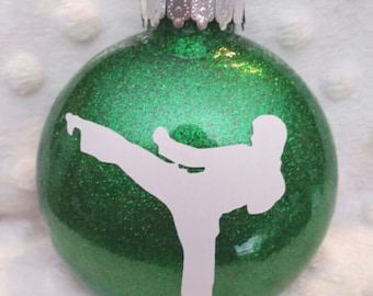 Könnte beinhalten: Grüner Glitzer-Weihnachtsbaumschmuck mit einer weißen Silhouette einer Person in Karate-Pose.