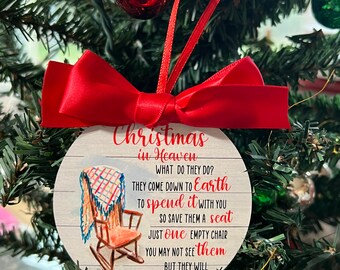 Könnte beinhalten: Ein runder, weißer Holzanhänger mit einem roten Band und einem Schaukelstuhl mit einer karierten Decke. Der Anhänger trägt den Text "Weihnachten im Himmel" und ein Gedicht darüber, dass geliebte Menschen auf die Erde kommen, um Weihnachten mit dir zu verbringen.