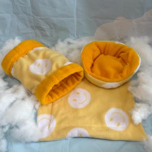 May include: A set of three yellow pet accessories: a bed, a tunnel, and a flat pad. Each item features a white smiley face pattern and bright yellow trim. The items are made of soft, plush material.
