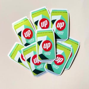 May include: A selection of stickers with a soda can design. The cans are light green with a red circle containing the word "up" in white. The text "ZERO SUGAR" is below the logo. The stickers have a modern design and the text "REFRESHING PUP TASTE ZERO SUGAR".