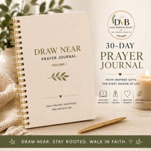 Può includere: Un diario di preghiera a spirale con copertina color crema, testo dorato che recita DRAW NEAR PRAYER JOURNAL VOLUME I, un grafico a foglia e le parole DAILY PRAYER, GRATITUDE AND REFLECTION, accompagnato da una penna dorata e una candela.