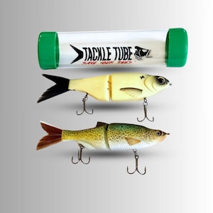 May include: Two fishing lures with treble hooks and a clear Tackle Tube with green end caps. The lures are designed to resemble fish, with detailed paint and realistic features. The Tackle Tube has the text "TACKLE TUBE" and "SAVE YOUR TAILS".