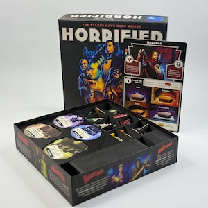 Puede incluir: El juego de mesa Horrified incluye una caja negra con ilustraciones de monstruos clásicos. En su interior, un inserto de plástico negro contiene fichas circulares y pequeñas figuras. Se incluye una tarjeta de personaje de Drácula con gráficos en rojo y negro.