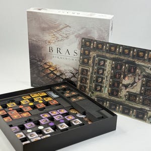May include: A Brass Birmingham board game set featuring a large rectangular game box with a sepia-toned industrial illustration, a black plastic storage tray filled with various coloured square game tiles, and a rectangular game board player mat.