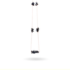 Puede incluir: Un conjunto de collar y pendientes de oro rosa. El collar presenta una hilera de piedras oscuras de forma irregular. Los pendientes tienen piedras similares suspendidas de delicadas cadenas. Las joyas se exhiben sobre un fondo blanco.