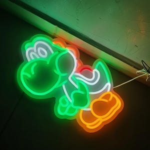 Pu&ograve; includere: Un'insegna al neon a forma di Yoshi, un personaggio di dinosauro verde della serie di videogiochi Super Mario. L'insegna ha un contorno verde con dettagli bianchi, arancioni e rossi. L'insegna &egrave; illuminata su uno sfondo scuro.