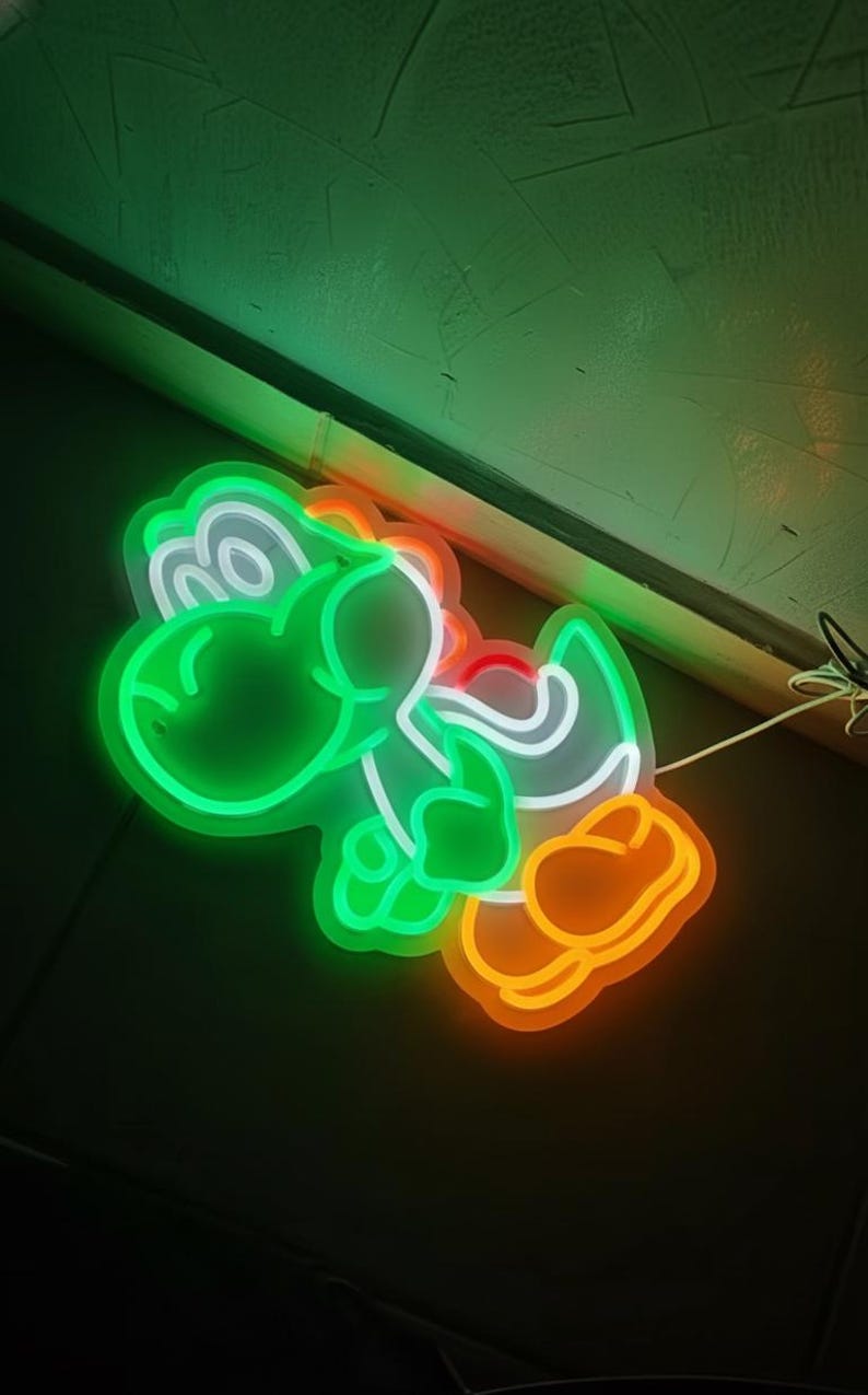 Pu&ograve; includere: Un'insegna al neon a forma di Yoshi, un personaggio di dinosauro verde della serie di videogiochi Super Mario. L'insegna ha un contorno verde con dettagli bianchi, arancioni e rossi. L'insegna &egrave; illuminata su uno sfondo scuro.
