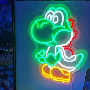 Pu&ograve; includere: Un'insegna al neon a forma di Yoshi, un personaggio di dinosauro verde. L'insegna ha un contorno verde con dettagli bianchi, rossi e gialli. &Egrave; montata su un muro blu.