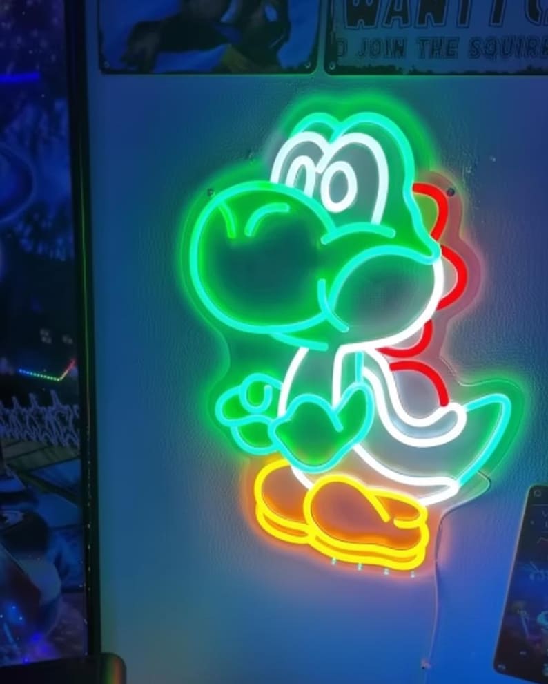 Pu&ograve; includere: Un'insegna al neon a forma di Yoshi, un personaggio di dinosauro verde. L'insegna ha un contorno verde con dettagli bianchi, rossi e gialli. &Egrave; montata su un muro blu.
