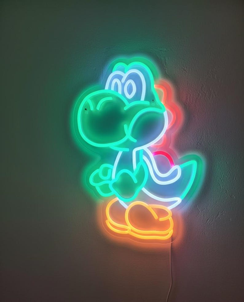 Pu&ograve; includere: Insegna al neon a forma di personaggio di dinosauro dei cartoni animati, con contorno verde e interno blu. Il dinosauro ha i piedi arancioni e un accento rosso sulla schiena. L'insegna &egrave; collegata alla parete.