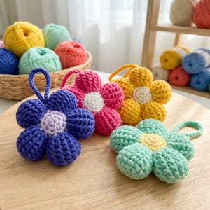 May include: Three crocheted flower ornaments with loops for hanging. One is dark blue with a light purple centre, one is bright pink with a white centre, and one is light green with a yellow centre. Each flower has six rounded petals.