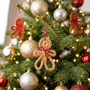 May include: A tan crocheted gingerbread person ornament hanging from a red string on a Christmas tree. The ornament features a circular head, looped arms and legs, and a small red bow tied at the neck. Other gold and red ornaments are visible.
