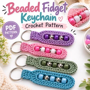 May include: Four crochet fidget keychains with metal rings, each featuring a row of colorful plastic beads separated by silver-toned metallic beads. The keychains are purple, pink, olive green, and light blue. Text reads Beaded Fidget Keychain Crochet Pattern.