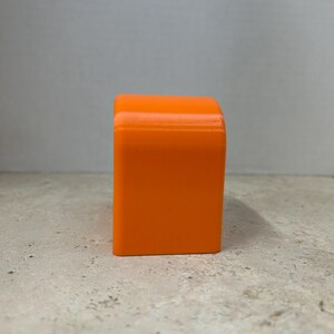 Peut inclure: Un objet rectangulaire orange vif avec des bords sup&eacute;rieurs arrondis. L'objet est d'une teinte orange vibrante et semble &ecirc;tre fait d'un mat&eacute;riau solide. Il est pos&eacute; sur une surface de couleur claire.