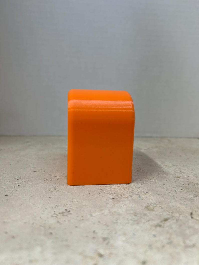 Peut inclure: Un objet rectangulaire orange vif avec des bords sup&eacute;rieurs arrondis. L'objet est d'une teinte orange vibrante et semble &ecirc;tre fait d'un mat&eacute;riau solide. Il est pos&eacute; sur une surface de couleur claire.