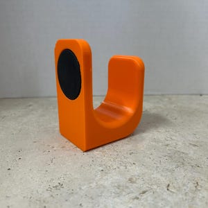 Peut inclure: Un objet orange en forme de U avec un &eacute;l&eacute;ment circulaire noir sur un c&ocirc;t&eacute;. L'objet est fait d'un mat&eacute;riau solide et a une finition lisse et mate. Le design est simple et moderne, adapt&eacute; &agrave; diverses utilisations.