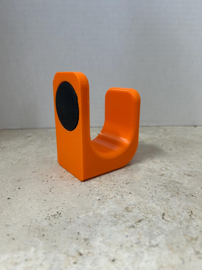 Peut inclure: Un objet orange en forme de U avec un &eacute;l&eacute;ment circulaire noir sur un c&ocirc;t&eacute;. L'objet est fait d'un mat&eacute;riau solide et a une finition lisse et mate. Le design est simple et moderne, adapt&eacute; &agrave; diverses utilisations.