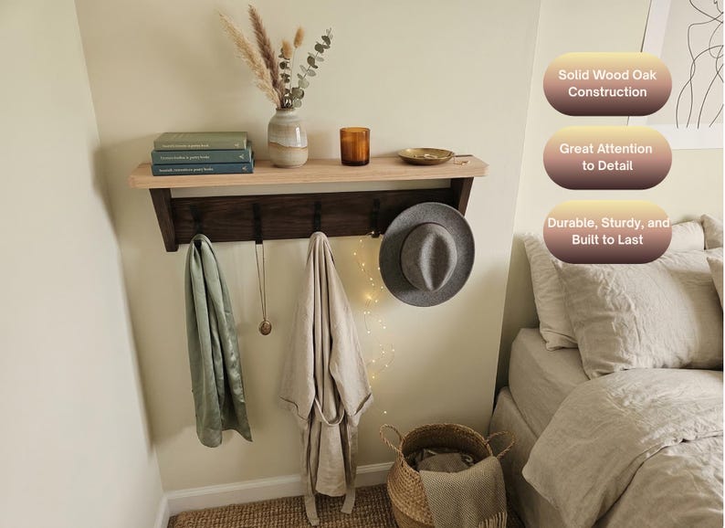 May include: A wall-mounted shelf with a light wood top and a dark wood base featuring four black metal hooks. The shelf holds books, a vase with dried plants, a candle, and a small dish. Text on the image reads: Solid Wood Oak Construction, Great Attention to Detail, Durable, Sturdy, and Built to Last.
