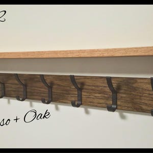 May include: A wall-mounted wooden shelf with a natural oak top and a dark espresso-stained backboard featuring seven black metal hooks. The text Code 12 and Espresso + Oak are visible, along with a circular logo reading NILSA PRAIRIE.
