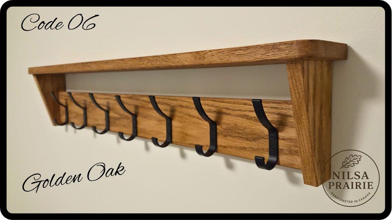 May include: A wall-mounted golden oak shelf featuring seven black metal hooks attached to a horizontal wooden board. The text Code 06 is visible in the top left, Golden Oak in the bottom left, and a circular logo for Nilsa Prairie in the bottom right.